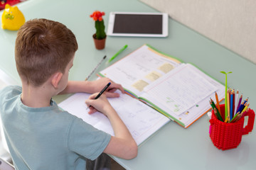 Distance learning online education. Schoolboy studying at home and doing school homework. Sitting chair with training books