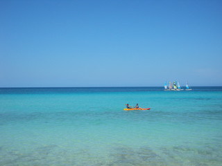 Fototapeta na wymiar Mar turquesa paradisíaco con dos personas en bote a remo y barcas de vela
