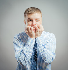 Closeup portrait of young man in blue shirt biting his nails and looking at you with a craving for something or anxious, isolated on white background, space to left. Negative Human facial expressions.