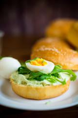 Homemade bun with cheese spread, fresh arugula and boiled egg in a plate