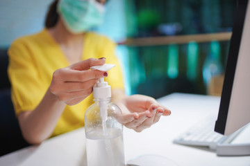 Business woman working with laptop on couch and wearing medical mask. Work from home. Concept prevention COVID-19, Coronavirus outbreak situation. Cleaning her hands with sanitizer gel.