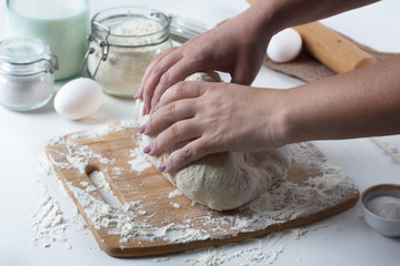 woman kneads dough with wheat flour on the table, next to the ingredients, baking