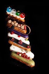 Close-up of Assorted eclairs with cream filling and elegant decorative toppings for confectionary photography concept in black background.