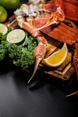 Delicious sea delicacy. King crab claws with greens, limes and oranges on wooden desk. Vertical shot. Close-up.