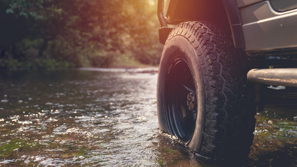Part of the mud-wheeled off-road opto-trailer parked in a stream with running water. with warm light. © PIPAT
