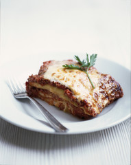 Beef lasagna of a traditional made with sauce topped with basil leaves served on a white plate - Close-up