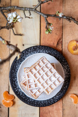 gebackene Waffeln mit Puderzucker und Früchten auf Brettern aus Holz mit schwarzem Hintergrund