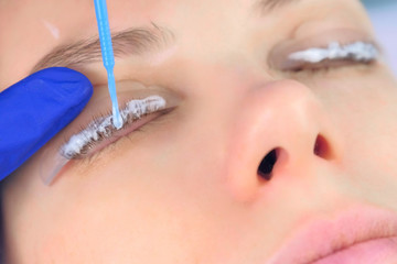 Beautician applying solution for lamination on woman lashes on curlers, lift eyelashes procedure in beauty salon, face closeup. Cosmetologist making lash lifting in cosmetology clinic, hands closeup.