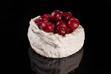 Meringue dessert with berries on top. Glossy black table
