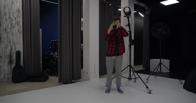 Young handsome male professional photographer taking photos of a model in a studio. He is pleased with the captured images. Digital camera DSLR.