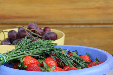 Summer. Fresh berries and herbs in the country. Strawberries in a blue bowl, a bunch of dill and dark grapes on a wooden background. Background image, copy space