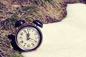 Old retro alarm clock, grass and snow, symbolizes the arrival of spring or winter.