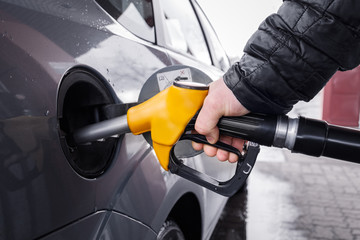 A man's hand holds a yellow refueling gun inserted into the opening of the car's gas tank when...