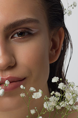 Fototapeta premium Close up half portrait of a face with beautiful skin and nude makeup, eyeliner and long eyelashes, puffy natural lips and white flowers. Fashion photography. Cosmetology and spa. Freshness of spring