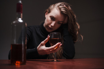 Young beautiful woman in severe depression, drinking alcohol. The concept of abuse and alcoholism. Alcoholic woman drinking from a bottle and glass of wine. Selective focus on glass.