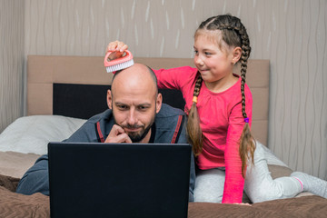 A little girl combs her bald dad with a brush. A child prevents a man from working on a laptop. The...