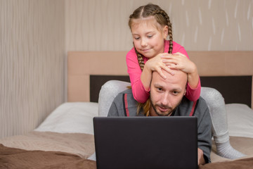 The child sat on top of the father and holds his head. The family is in quarantine. A little girl...