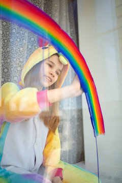 Child Girl In Kigurumi Draws Rainbow On Window.