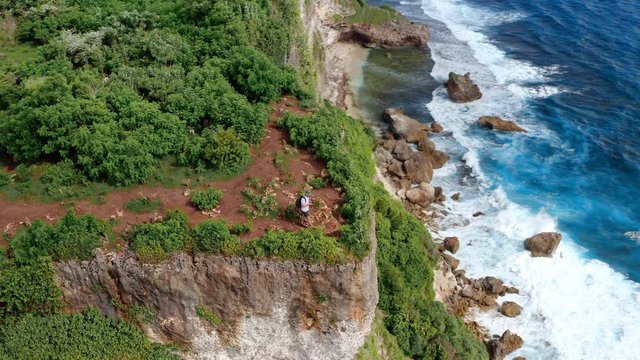 Aerial drone view of happy sporty plus size man traveler use his mobile device smartphone on a mountain cliff. Guy use online or offline maps and GPS satellites for travelling with navigation device.
