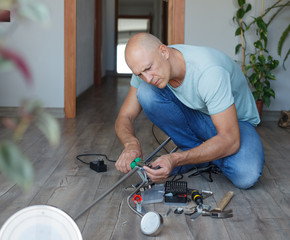 A man repairs a floor lamp while sitting on the floor of a house