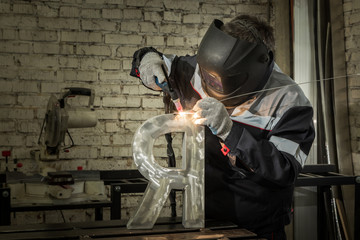 Welder welding a metal part in an industrial environment, wearing standard protection equipment.