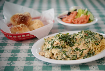 Spinach chicken pasta white sauce with garlic rolls and salad on the table