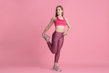Fototapeta na wymiar Stretching. Beautiful young female athlete practicing in studio, monochrome pink portrait. Sportive fit caucasian model training. Body building, healthy lifestyle, beauty and action concept.