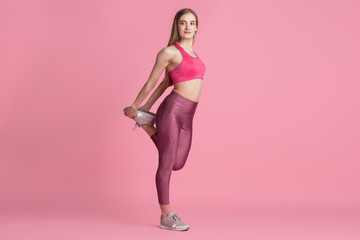 Fototapeta na wymiar Stretching. Beautiful young female athlete practicing in studio, monochrome pink portrait. Sportive fit caucasian model training. Body building, healthy lifestyle, beauty and action concept.