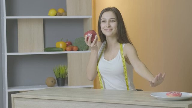 Caucasian girl looks at the table with pleasure to eat an apple and pushes gingerbread