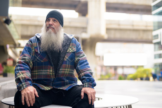 Mature handsome bearded man thinking and sitting in the city outdoors