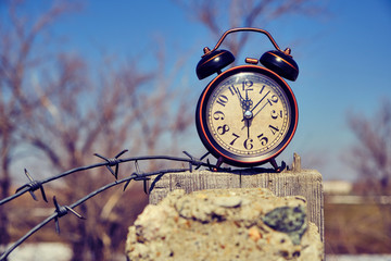 Old retro alarm clock on post tied with barbed wire symbolizes arrival of spring.