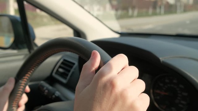 Close up view of woman hands holding steering wheel driving a car on city street on sunny day.