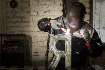 Obraz na płótnie Canvas Welder welding a metal part in an industrial environment, wearing standard protection equipment.