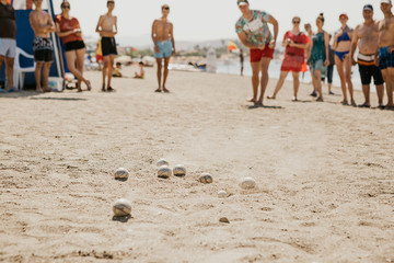 Portrait of friendly people playing petanque at leisure on the beach near a hotel full of vacationers