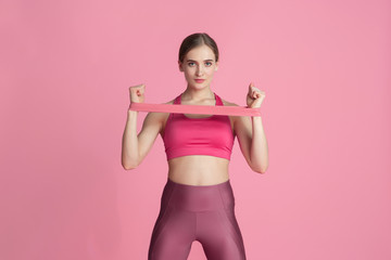 Upper body. Beautiful young female athlete practicing in studio, monochrome pink portrait. Sportive fit caucasian model with elastics. Body building, healthy lifestyle, beauty and action concept.