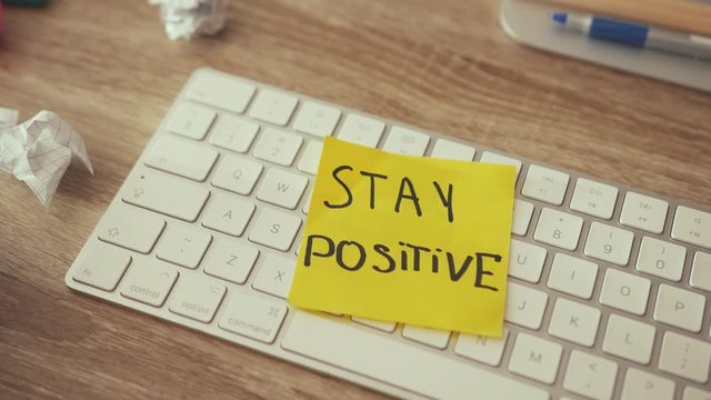 Creative clutter on wooden table desktop. Home office disorder. Lack of motivation. Inspiring note sticker text saying to Stay Positive. Business, inspiration.