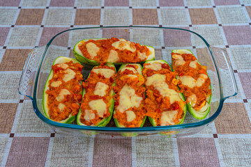 Zucchini stuffed with minced meat, cheese and mushrooms. Oven baked. The zucchini are in a glass bowl. On a square tablecloth table.