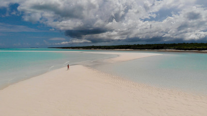 Aerial drone view of a woman walking alone trough a sandbank near to the clear blue water of Indian Ocean 