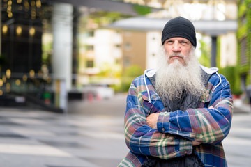 Mature bearded hipster man with arms crossed in the city streets outdoors