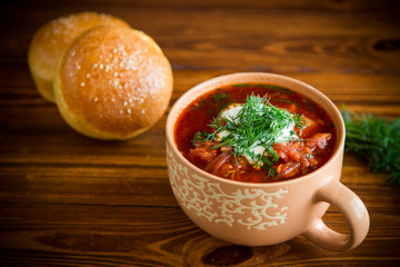 hot beetroot soup with sour cream, herbs and rolls in a ceramic bowl