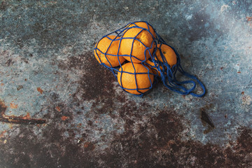 Oranges in an eco-netted blue bag on a dark background. Environmental care, waste recycling.