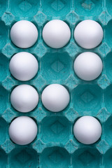 Full colourful teal egg carton box with white chicken eggs forming a 'R' well lit in studio lighting