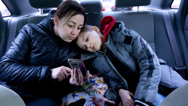 Mom Shows Her Son A Photo On Her Phone. In The Back Of The Car