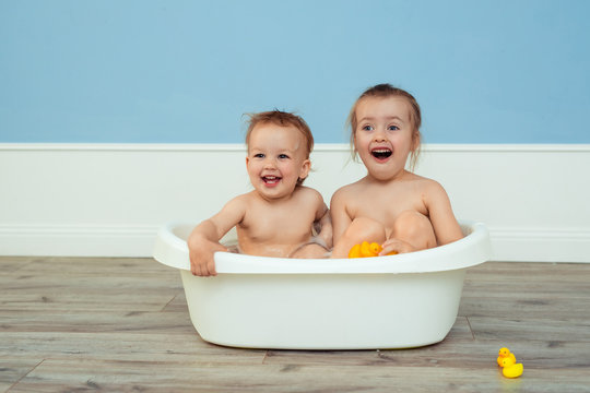 baby bathing and hygiene. care for young children. two cheerful sisters bathe in a white baby bath and play among the soap suds