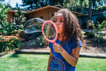 Happy girl blowing giant bubbles in the front yard of home
