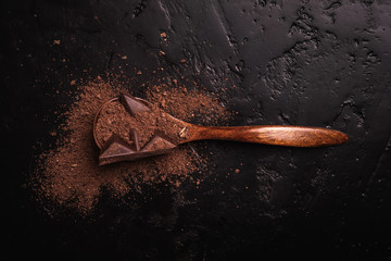 In a wooden spoon, a chocolate bar and chocolate chips, cocoa beans, cocoa powder, cocoa butter, a chocolate bar on a dark background place for text