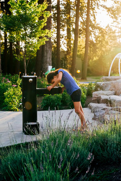 Girl Drinking At Water Fountain In Public Park At Sunset