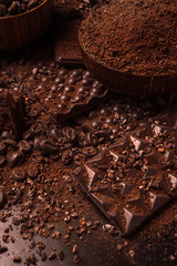 Cocoa beans, cocoa powder, cocoa butter, chocolate bar and chocolate sauce, chocolate bar in a wooden bowl on a dark background place for text