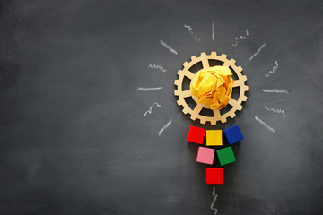 Education concept image. Creative idea and innovation. Wooden gears light bulb metaphor over blackboard