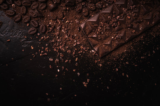 Cocoa beans, cocoa powder, cocoa butter, chocolate bar and chocolate sauce, chocolate bar in a wooden bowl on a dark background place for text